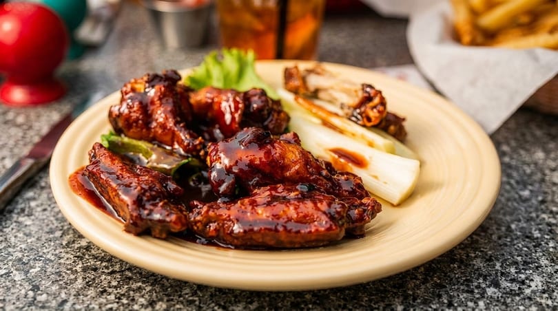 Plate of BBQ chicken wings with grilled scallions and lettuce on a speckled table.